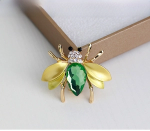 Detailed close-up of a golden bee brooch with a green gemstone and rhinestones in a gift box