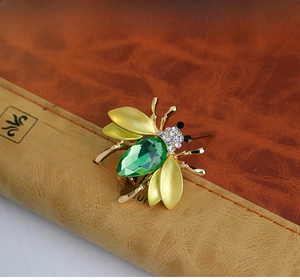 Macro detail of bee brooch with green crystal gem and gold-tone matte wings