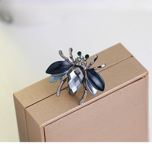 Detail of bee brooch with dark grey crystals and green eyes on metallic box
