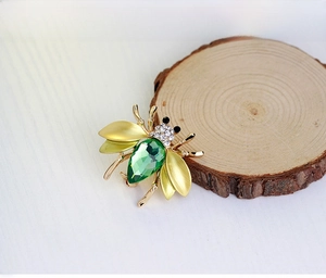 Macro detail of bee brooch with green crystal teardrop and gold wings on wood background