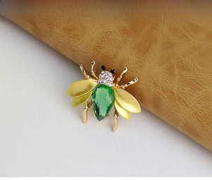 Close-up of a bee brooch with a large green teardrop gemstone and matte gold wings