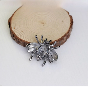 Detailed rear view of metal bee brooch with pin clasp on a natural wood slice stand