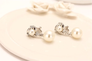 Macro shot of elegant silver pearl clip-on earrings with zircon on a ceramic tray