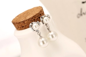 Macro shot of elegant silver pearl earrings with crystals on a white ceramic vase