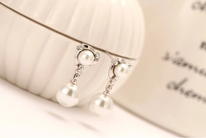 Macro shot of silver pearl stud earrings with sparkling diamonds and windmill spiral design