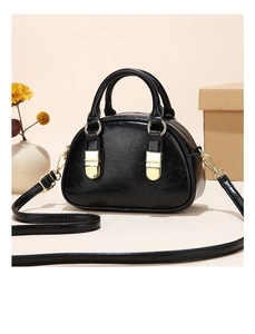 Detailed close-up of glossy black PU leather handbag with golden metal buckles on beige background