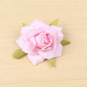 Pink artificial rose head with glitter edges and silk leaves on light wood background