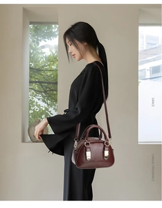 Detail of burgundy glossy leather bowling bag featuring golden hardware and top handles