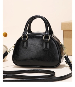 Detail of black glossy patent leather handbag with pleated texture and gold hardware