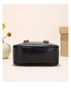 Detail view of the black glossy bag base with golden hardware and neat stitching