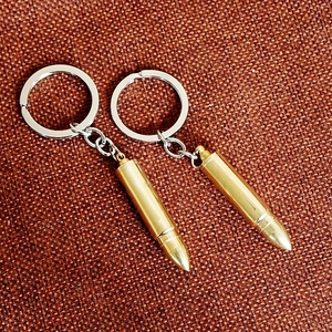 Pair of golden bullet-shaped metal keychains on textured brown fabric background