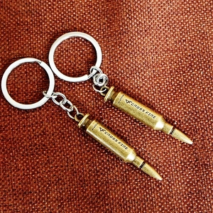 Detailed macro view of two bronze-finish bullet-shaped metal keychains on textured fabric