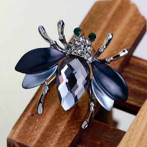 Fashion insect brooch with grey crystal body and green gem eyes on a wooden base