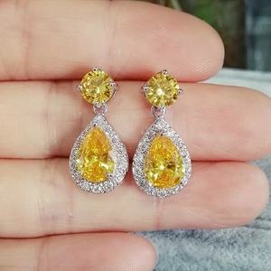 Macro shot of yellow teardrop zircon earrings with silver plating held by hand