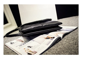 Détail du sac enveloppe noir en cuir grainé avec chaîne argentée sur magazine de mode