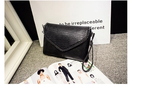 Détail d'une pochette enveloppe noire en relief crocodile avec chaîne en métal