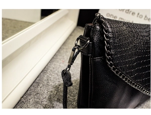 Gros plan du sac enveloppe noir avec texture crocodile et bandoulière en chaîne