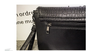 Détail d'un sac à main en cuir noir avec rabat motif crocodile et fermeture éclair
