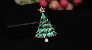 Close-up of green enamel Christmas tree brooch with colorful rhinestones on a jewelry box