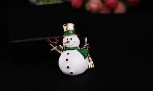 Detail of a Christmas snowman brooch with enamel finish next to a black jewelry box