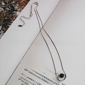Silver snake chain necklace with black onyx bead pendant resting on an open book