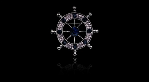 Detail view of silver ship wheel brooch with purple and deep blue rhinestones on black base