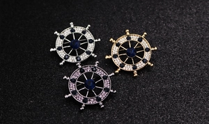 Macro detail of nautical ship wheel lapel pins with vibrant crystals on dark background