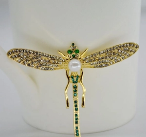 Detailed shot of golden dragonfly brooch with green crystals and white pearl on ceramic