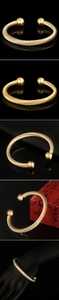 Detailed views of twisted gold-plated open bangles with solid bead ends on black background