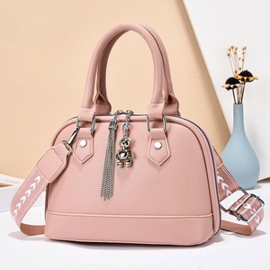 Pink lychee texture shell bag with wide shoulder strap and bear charm on geometric background