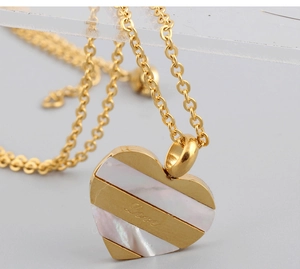 Close-up of heart necklace with white shell inlay and 'Love' engraving on gold metal