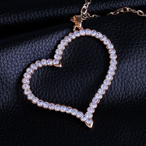 Close-up of gold hollow heart pendant with white crystals on black leather background