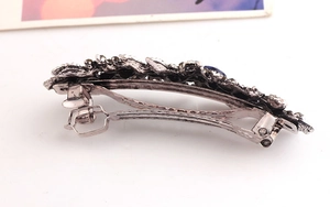 Detailed close-up of antique silver hair clip with blue gemstone and metal spring clip