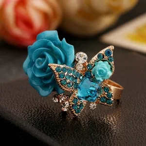 Detalle de anillo con rosa y mariposa con pedrería azul sobre banda dorada fina