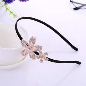 Elegant black headband with golden rhinestone flower accents on a clean white desk