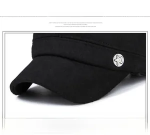 Detail of black winter flat top hat featuring a silver star metal button and stitching