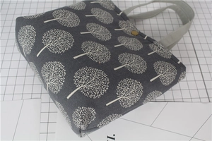 Detailed close-up of dark grey linen lunch bag with white tree prints and bronze button