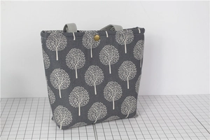 Detail of dark grey lunch bag with white tree patterns and golden metal snap button closure