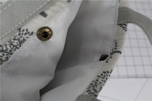 Macro detail of canvas lunch bag featuring bronze metal snap button and linen texture