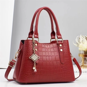 Sac à main rouge à motif crocodile avec poignées et breloque en perles sur table