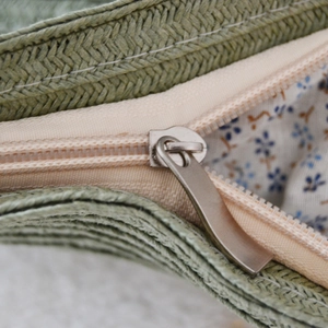 Detail of green straw woven texture with floral lining and silver metal zipper puller