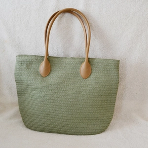 Detail of green woven tote bag featuring textured straw patterns and brown leather handles