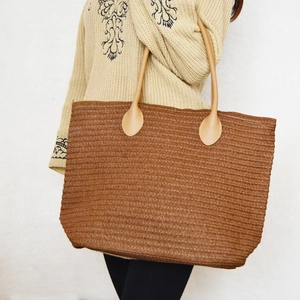 Close-up of woven straw tote bag texture and brown handles shown on female model