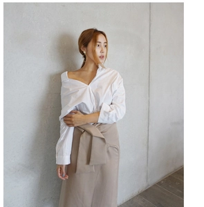 Detail of elegant white off-shoulder shirt and beige high-waisted wrap skirt set