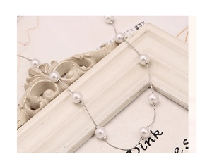Detailed view of white pearls on a slim silver metal chain over a vintage white frame