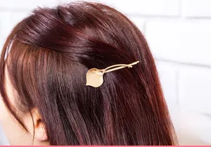 Detail of matte gold leaf hair clip with white pearl on soft reddish-brown wavy hair