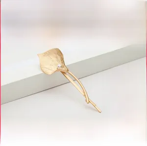 Detail view of a golden calla lily hair clip with a pearl on a white pedestal