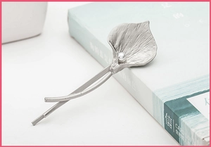 Detail of silver calla lily hair clip with pearl accent on light blue background