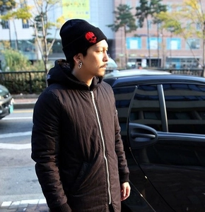Close-up of black knit beanie featuring red skull embroidery on a city street background