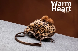 Detailed view of leopard print plush bucket bag with pom-poms and adjustable strap
